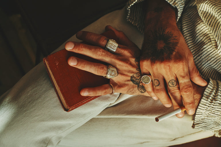 lifestyle photo image of male hands holding book and cigarette, wearing sterling silver souvenir biker and coin rings