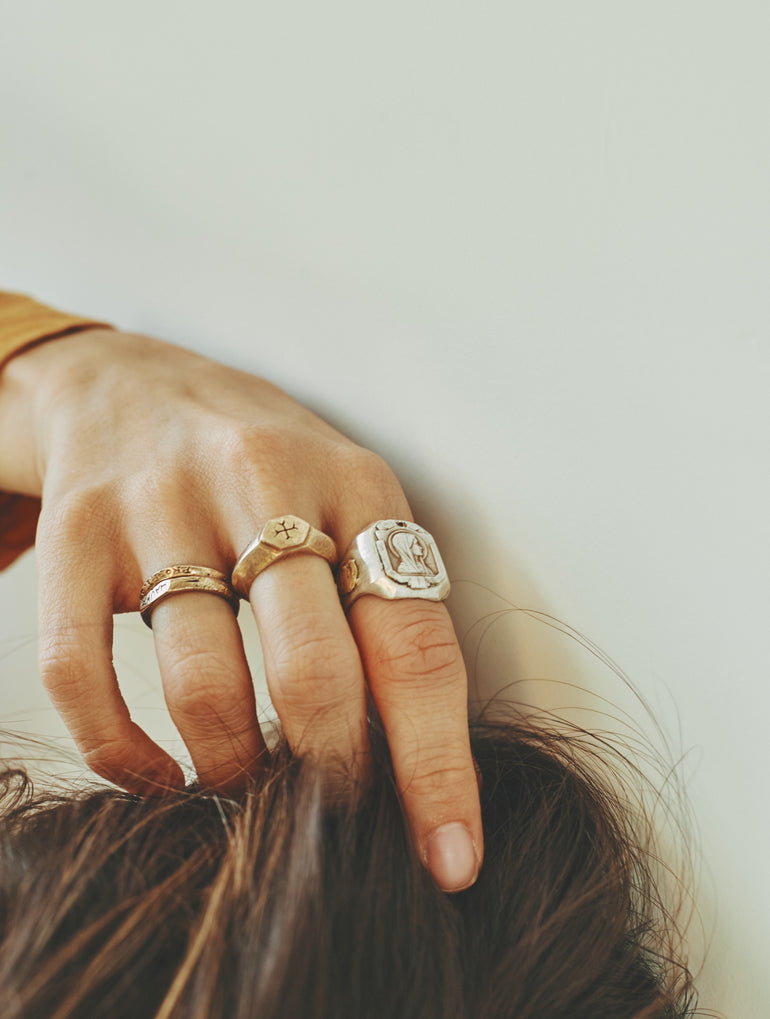 lifestyle photo image of hand in hair, hand wearing multiple silver and bronze rings, Mother Mary ring and Sacred Love ring